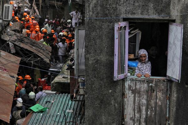 Местная жительница смотрит в окно, пока спасатели ищут выживших после обрушения здания в Мумбаи, Индия - Sputnik Абхазия