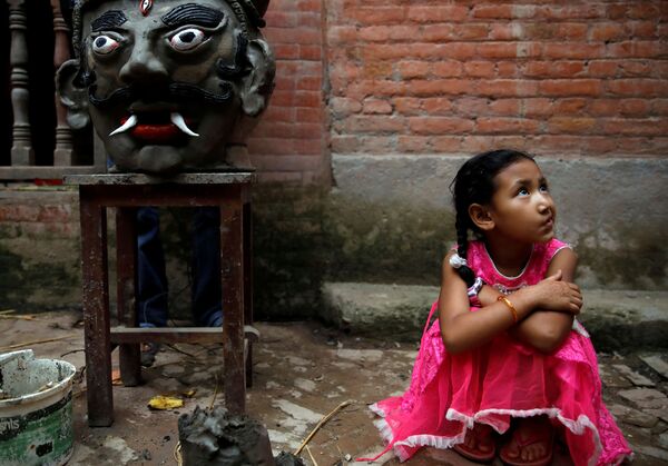 Девочка сидит рядом с головой демона Гхантакарны, прежде чем его сожгут на фестивале Гхантакарна, Непал - Sputnik Абхазия
