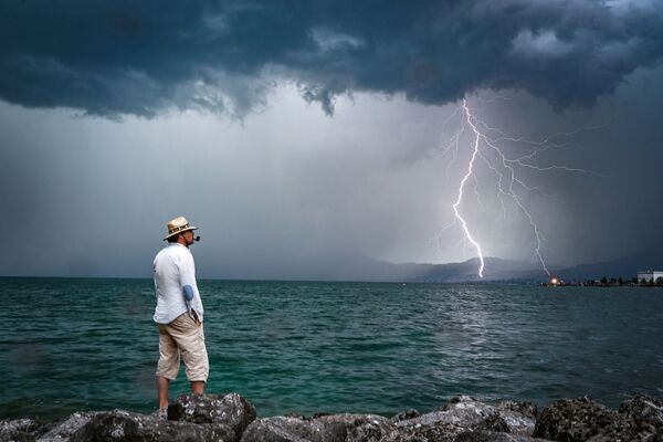 Мужчина на фоне молнии на горизонте озера Женева в Швейцарии - Sputnik Абхазия