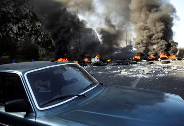 Мужчина спит в машине рядом с горящими шинами на шоссе во время продолжающихся антиправительственных акций протеста в Нар-эль-Кальб, Ливан - Sputnik Абхазия