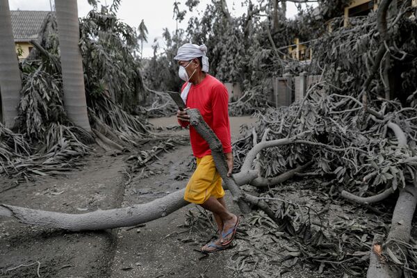 Мужчина убирает поваленные деревья после извержения вулкана Тааль на Филппинах - Sputnik Абхазия