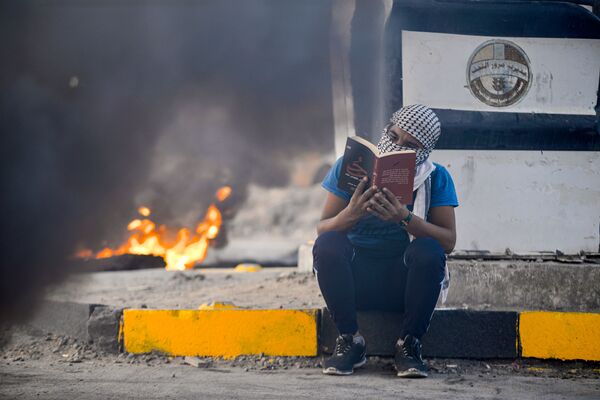 Участник антипровительственных протестов читает роман на фоне горящих шин, Эн-Наджаф, Ирак - Sputnik Абхазия
