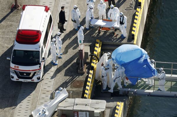 Сотрудники полиции в защитных костюмах помещают в машину скорой помощи заболевшего пассажира круизного лайнера Diamond Princes, помещенного в карантин у японского порта Йокогама - Sputnik Абхазия