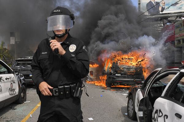 Полицейский Лос-Анджелеса на фоне горящей машины во время протестов  - Sputnik Абхазия