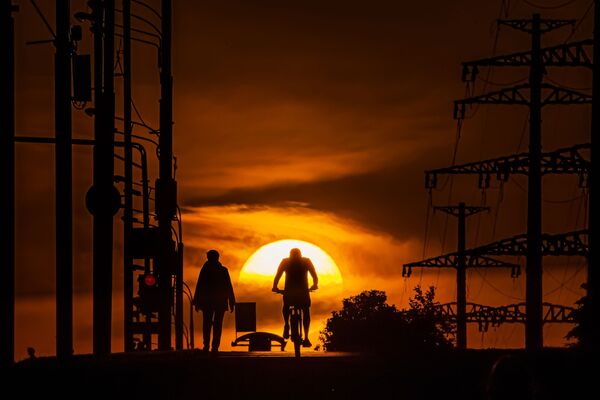 Мужчина едет на велосипеде по одной из улиц в Москве на фоне заката - Sputnik Абхазия
