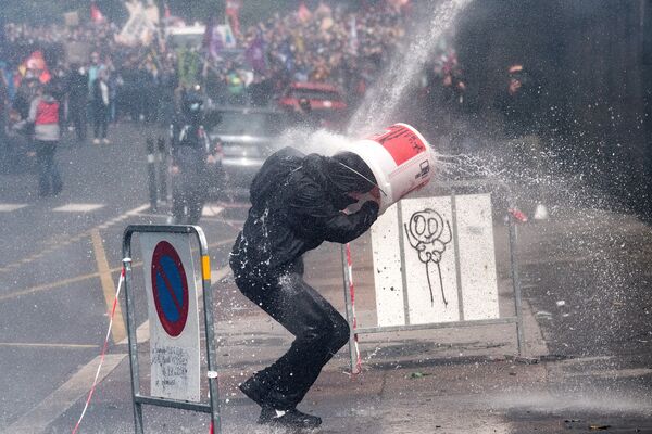 Протестующий прикрывается ведром от удара водяной пушкой, которую полицейские используют для разгона акции протеста медработников в Нанте, Франция - Sputnik Абхазия