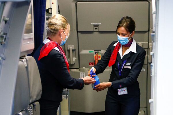 Стюардессы в медицинских масках обрабатывают руки антисептическим гелем в салоне самолета в международном аэропорту Брюсселя - Sputnik Абхазия