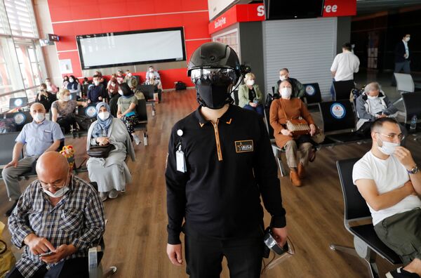 Сотрудник службы безопасности в тепловизионном шлеме следит за пассажирами, ожидающими посадки на рейс в аэропорту Стамбула - Sputnik Абхазия